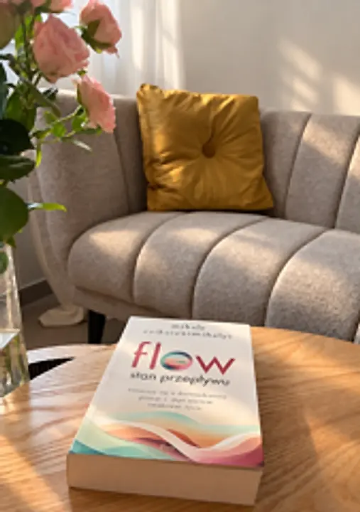 Książka „Flow. Stan przepływu” na stoliku, w tle sofa z musztardową poduszką i róże